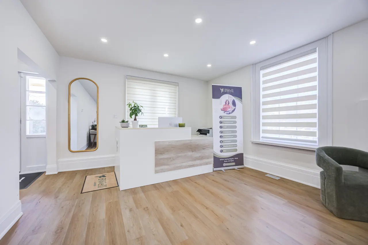 The reception at BWell Lounge: a white front desk with plants and a brass arched mirror