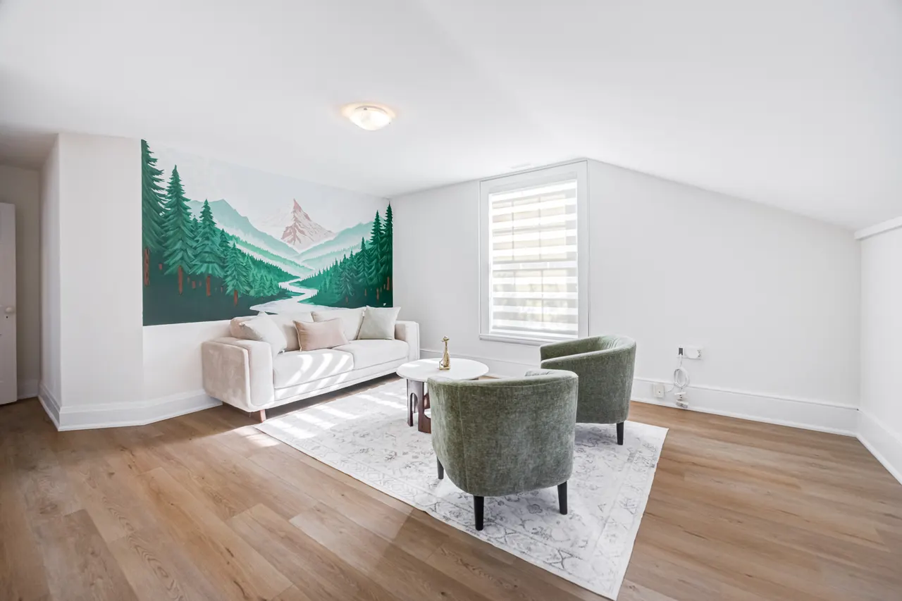 A room at BWell Lounge with a forest-and-mountain mural, a cream sofa and two green chairs