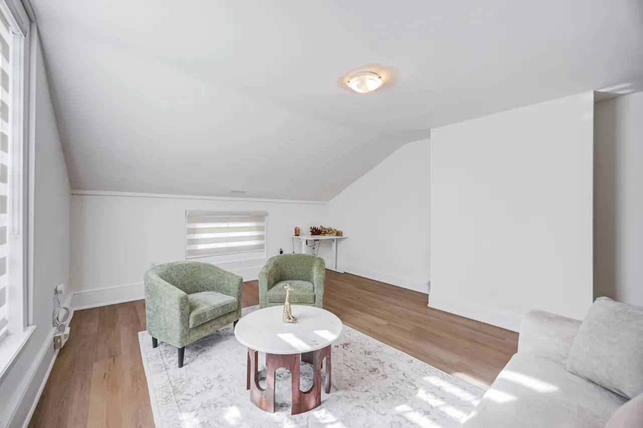 Two green armchairs around a small round table on a rug, in a bright upstairs room at BWell Lounge